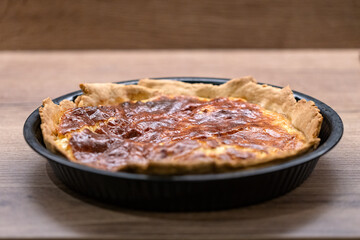 A quiche with fried smoked bacon and cheese in a pie pan on table.