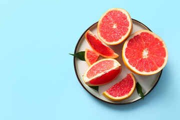 Plate with cut fresh grapefruits and leaves on blue background