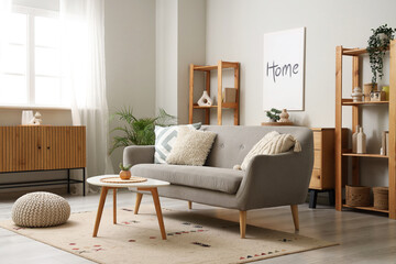 Interior of light living room with grey sofa, table and shelf units