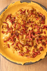 Dough with fried bacon and onion put in round pan to make a quiche. Baking at home.