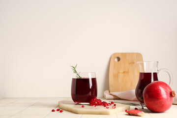 Glass and jug of fresh pomegranate juice with seeds on white tile table