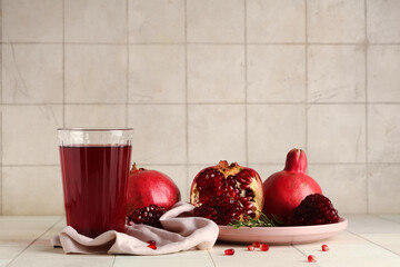 Glass of fresh pomegranate juice and plate with fruits on white tile background