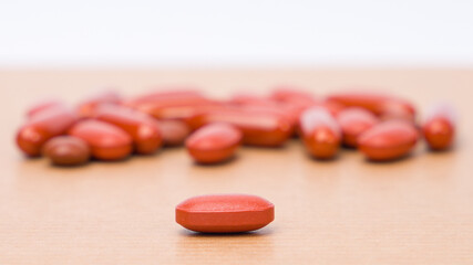 Red medicine pills on wooden table. Focus on foreground, shallow DOF.