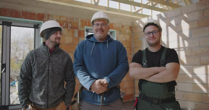 Three construction workers standing together indoors, wearing safety helmets, smiling and showing unity on an unfinished building site, representing teamwork and camaraderie
