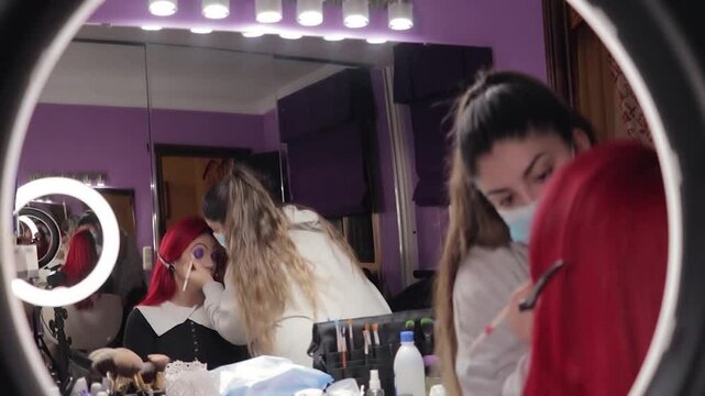 Makeup Artist Applying Character Makeup to Redhead Woman &ndash; Mid Shot Reflected in Mirror. Maquilladora Aplicando Maquillaje de Caracterizaci&oacute;n a Mujer Pelirroja &ndash; Plano Medio Reflejado en el Espejo
