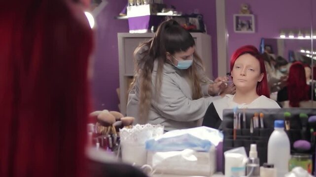Makeup Artist Applying Character Makeup to Redhead Woman &ndash; Mid Shot Reflected in Mirror. Maquilladora Aplicando Maquillaje de Caracterizaci&oacute;n a Mujer Pelirroja &ndash; Plano Medio Reflejado en el Espejo
