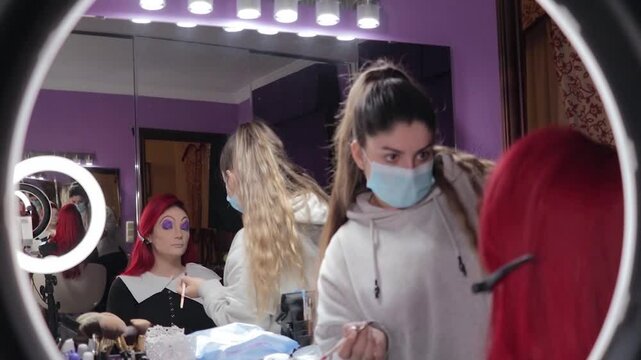 Makeup Artist Applying Character Makeup to Redhead Woman &ndash; Mid Shot Reflected in Mirror. Maquilladora Aplicando Maquillaje de Caracterizaci&oacute;n a Mujer Pelirroja &ndash; Plano Medio Reflejado en el Espejo
