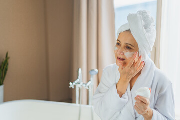 Mature adult old woman applying nourishing anti age face cream doing daily beauty routine. Senior...