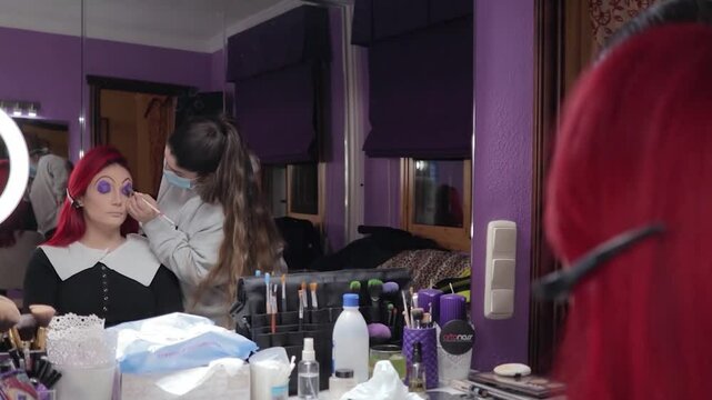 Makeup Artist Applying Character Makeup to Redhead Woman &ndash; Mid Shot Reflected in Mirror. Maquilladora Aplicando Maquillaje de Caracterizaci&oacute;n a Mujer Pelirroja &ndash; Plano Medio Reflejado en el Espejo
