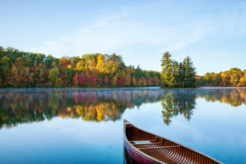 Red wood canoe on a beautiful calm lake with trees in fall color and a small island