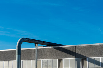 Fototapeta premium Metal pipe extends over the edge of a building under a clear blue sky