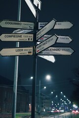 A multi-directional signpost at night in Elbląg, Poland, displays distances to various...