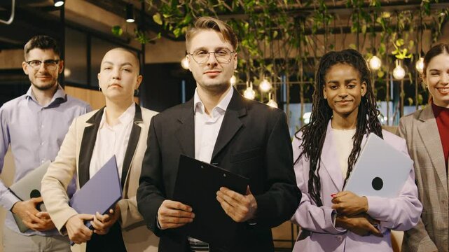 Multiracial team of business professionals stands in a row, smiling confidently for a corporate portrait, showcasing unity, leadership, and professional camaraderie.
