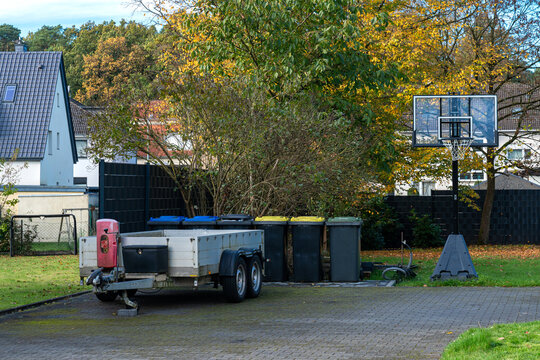 Outdoor basketball hoop beside a trailer and trash bins on a sunny day