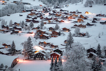Grindelwald, under the soft glow of the night lights, transforms into a magical village where the snow glistens and each chalet seems to watch over the peaceful, slumbering mountains, Switzerland.