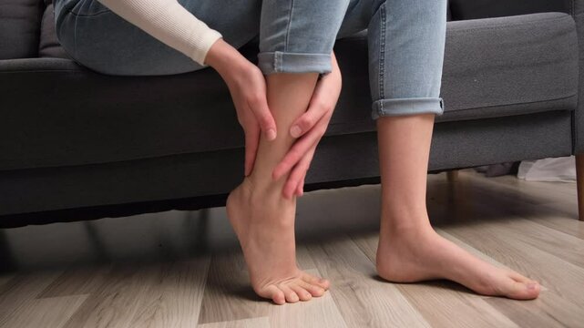 Muscle pain or leg pain. Suffer young caucasian woman massaging brawn leg calf muscle cramps or spasm, trauma from inflammation of tendon at calves while sitting alone on sofa. Health care concept