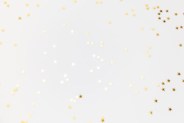 Gold sparkle confetti stars on a white background. Glitter, shine, bright. Christmas festive flat lay, winter holiday, new year, happy birthday concept. Banner for greeting card, top view, copy space.