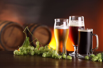 Glasses with different types of beer and fresh hops on wooden table in bar. Space for text
