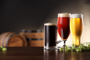 Glasses with different types of beer and fresh hops on wooden table in bar. Space for text