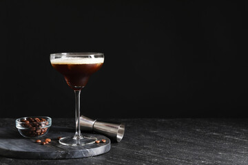 Glasses of delicious espresso martini, jigger and coffee beans on dark textured table, closeup. Space for text