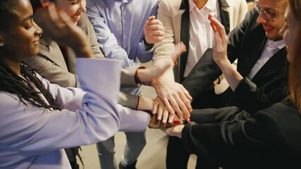 A close-up of joyful, diverse business professionals holding hands in unity, showing teamwork and a strong sense of camaraderie in a modern loft office.