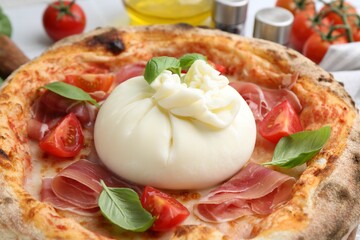 Delicious pizza with burrata cheese, basil, tomatoes and ham on table, closeup