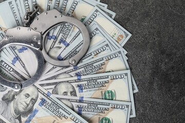 Corruption concept. Handcuffs and dollar banknotes on grey table, top view
