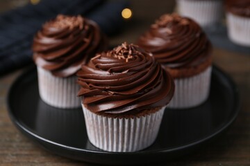 Tasty cupcakes with chocolate cream on wooden table, closeup