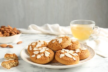 Tasty cookies with almond flakes, nuts and tea on white marble table, closeup