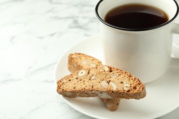 Traditional Italian almond biscuits (Cantucci) and mug of coffee on white marble table, closeup. Space for text