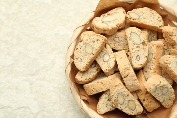 Traditional Italian almond biscuits (Cantucci) in wicker bowl on light textured table, top view. Space for text
