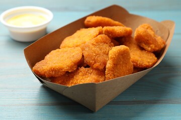 Delicious chicken nuggets in carton box on blue wooden table, closeup
