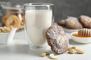 Tasty chocolate cookie with cashew and glass of milk on white table, closeup