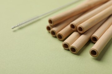 Bamboo drinking straws and cleaning brush on green background, closeup