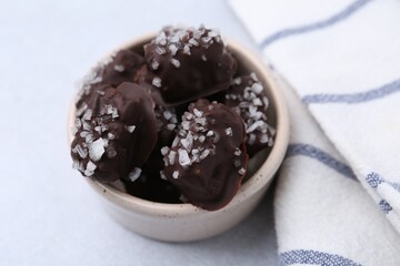 Tasty chocolate candies with salt in bowl on light table, closeup