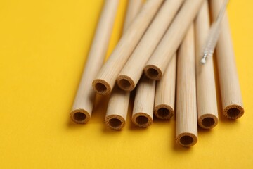 Bamboo drinking straws and cleaning brush on yellow background, closeup
