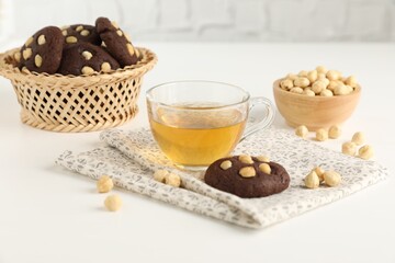 Tasty chocolate cookies with hazelnuts and tea on white table, closeup