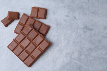 Pieces of delicious milk chocolate on grey table, top view. Space for text