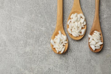 Puffed rice in wooden spoons on light grey table, flat lay. Space for text