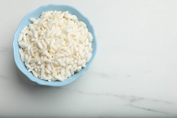 Puffed rice in bowl on white marble table, top view. Space for text