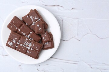 Pieces of chocolate with salt on white table, top view. Space for text