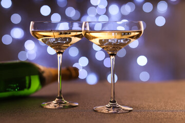 Champagne in glasses and bottle on table against blurred lights, closeup