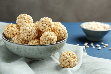 Tasty puffed rice balls in bowl on blue table, closeup