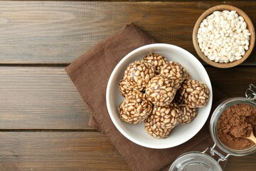 Tasty chocolate puffed rice balls in bowl and ingredients on wooden table, flat lay. Space for text