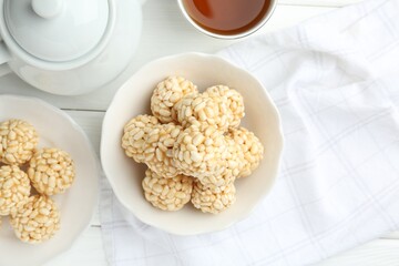 Tasty puffed rice balls and tea on white wooden table, flat lay