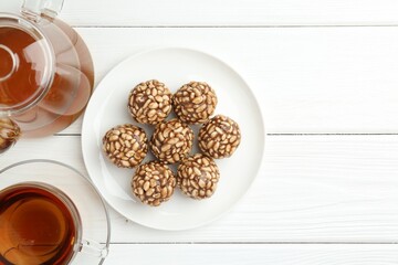 Tasty chocolate puffed rice balls and tea on white wooden table, flat lay. Space for text