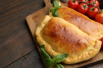 Tasty vegetarian calzones with basil and tomatoes on wooden table, closeup. Space for text