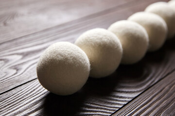 Wool dryer balls arranged in a row on a dark, textured wooden surface with visible grain, perfect for eco-friendly laundry care