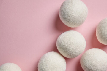 White wool dryer balls scattered on a pastel pink background, with visible wool texture. This eco-friendly arrangement conveys a minimalist and sustainable home care vibe