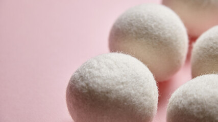 Close-up of white wool dryer balls on a pastel pink background, showcasing their soft, fluffy texture. This minimalist arrangement highlights sustainable laundry essentials